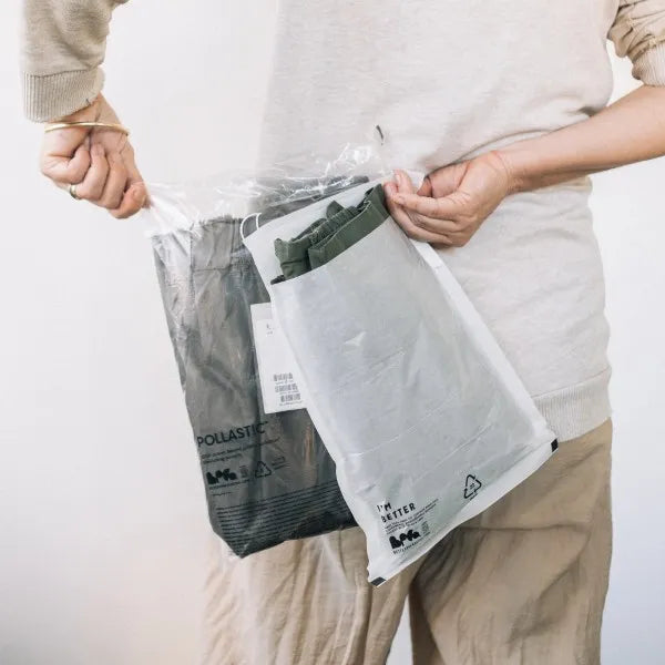 Person holding a POLLAST!C Poly Garment Bag and Glassine Garment Bag behind their back