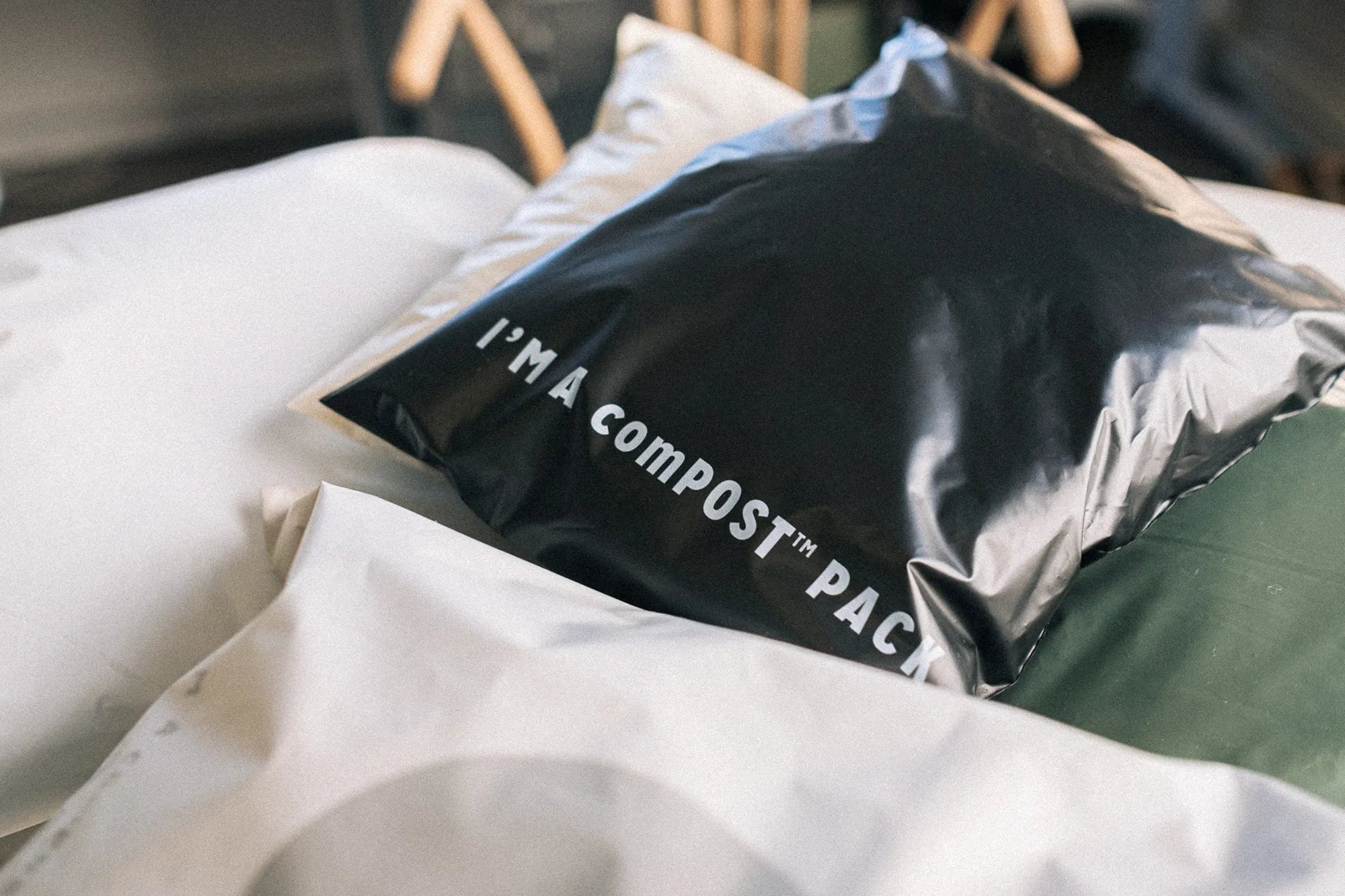 A black compostable mailer with white text "I'M A comPOST™ PACK" sits on top of two other packages.